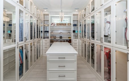 A recently-remodeled closet featuring large storage with high-end finishes, such as glass-front cabinets.